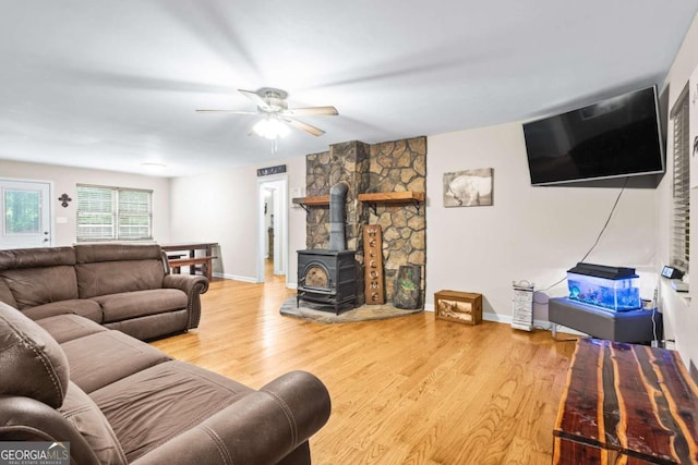 living room with wood-type flooring, a wood stove, and ceiling fan