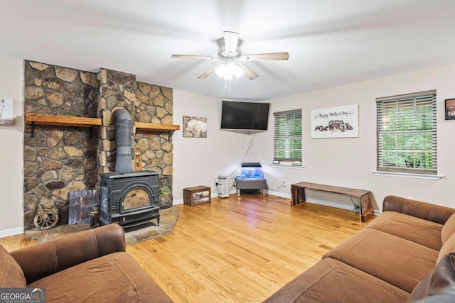 living room with wood-type flooring, ceiling fan, and a wood stove