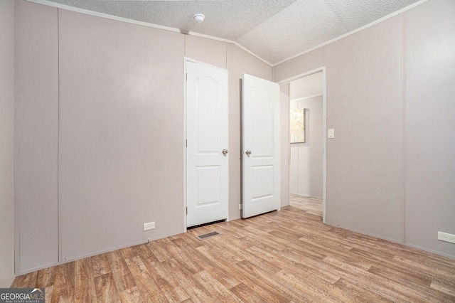 unfurnished bedroom with light hardwood / wood-style floors, ornamental molding, a textured ceiling, and vaulted ceiling