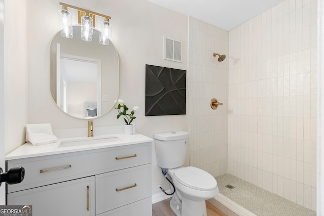 bathroom with tiled shower, vanity, hardwood / wood-style flooring, and toilet