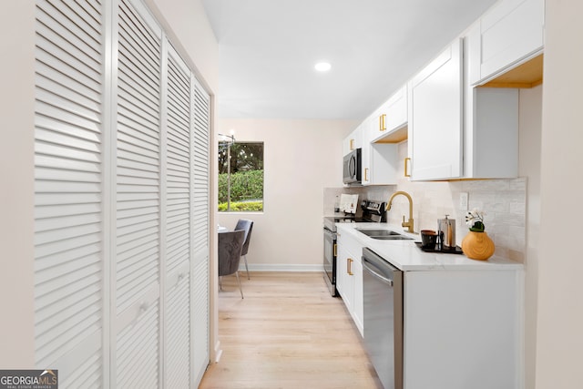 kitchen featuring sink, light hardwood / wood-style flooring, appliances with stainless steel finishes, tasteful backsplash, and white cabinetry