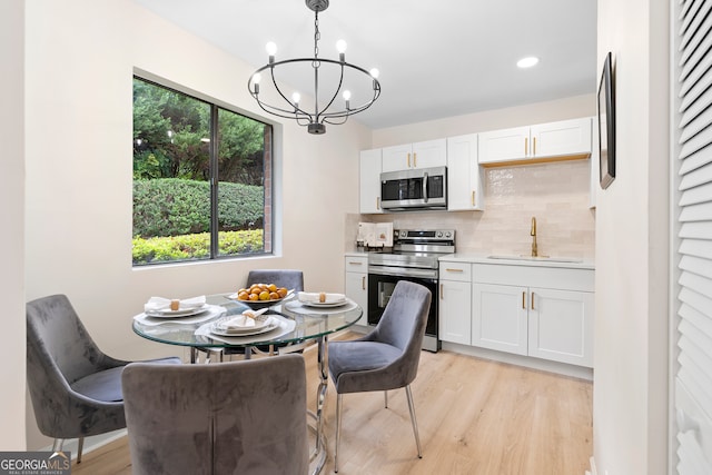 kitchen featuring white cabinets, hanging light fixtures, sink, light hardwood / wood-style flooring, and appliances with stainless steel finishes