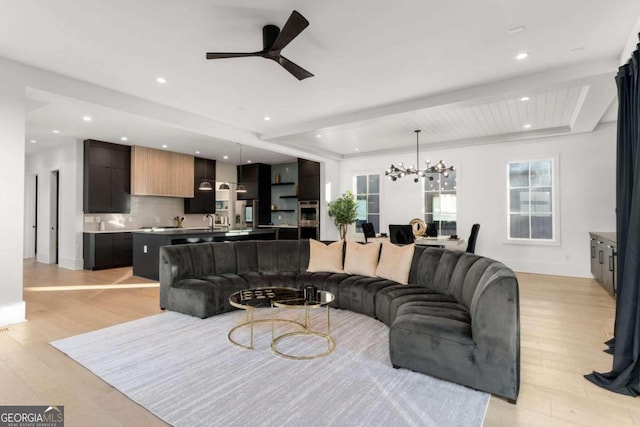 living room featuring ceiling fan with notable chandelier, light wood-type flooring, and sink