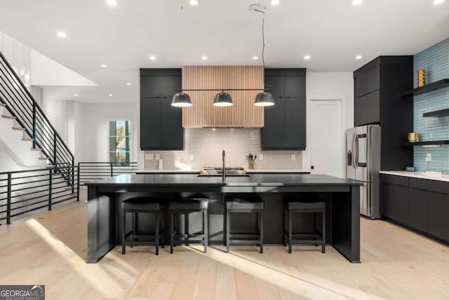 kitchen with backsplash, a breakfast bar, an island with sink, and stainless steel refrigerator with ice dispenser