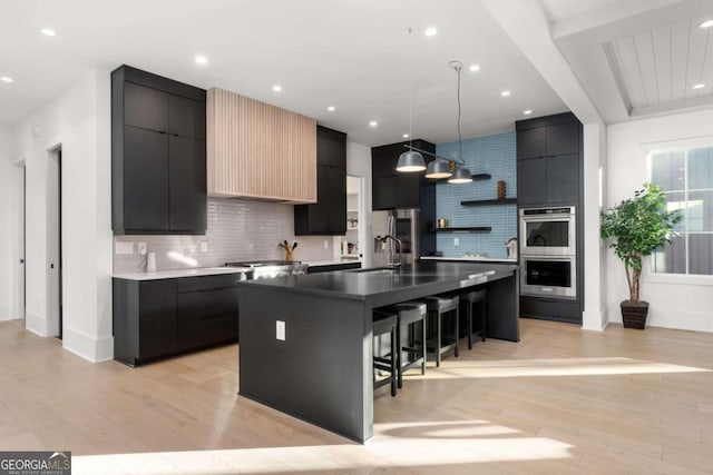 kitchen with a kitchen breakfast bar, light hardwood / wood-style flooring, an island with sink, tasteful backsplash, and decorative light fixtures