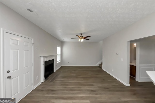 unfurnished living room featuring dark hardwood / wood-style floors, ceiling fan, and a textured ceiling