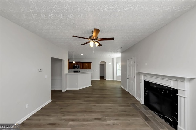 unfurnished living room featuring a textured ceiling, ceiling fan, and dark wood-type flooring