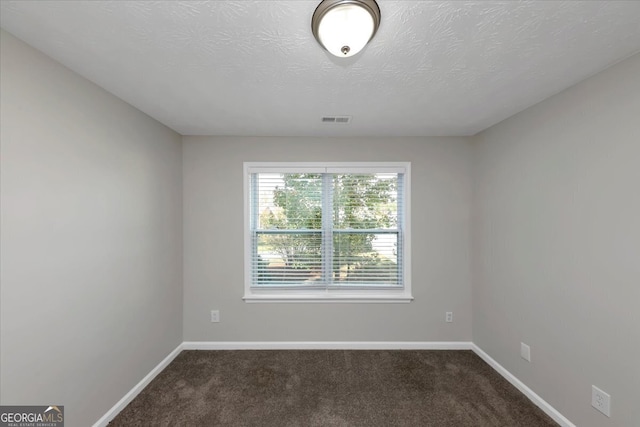 empty room with dark carpet and a textured ceiling