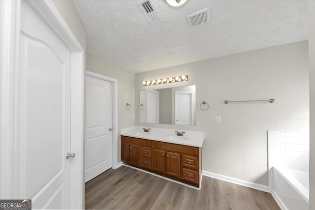 bathroom with vanity, a textured ceiling, hardwood / wood-style flooring, and a tub