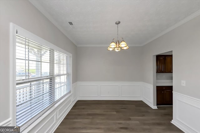 unfurnished dining area with a textured ceiling, crown molding, dark wood-type flooring, and a chandelier