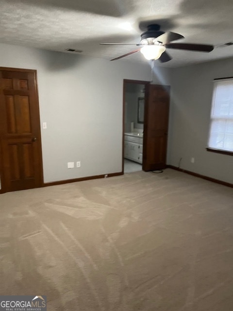 unfurnished bedroom featuring light carpet, a textured ceiling, ensuite bath, and ceiling fan