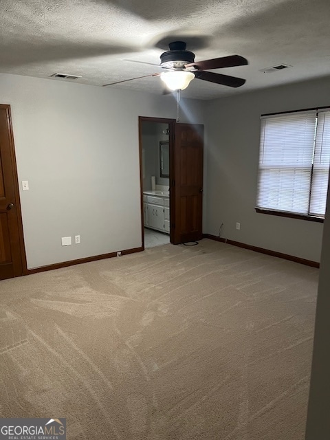 unfurnished bedroom featuring ceiling fan, light colored carpet, a textured ceiling, and connected bathroom