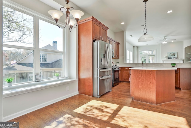 kitchen with ceiling fan with notable chandelier, appliances with stainless steel finishes, decorative light fixtures, light hardwood / wood-style floors, and kitchen peninsula