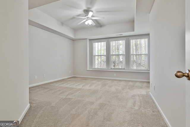 empty room featuring light colored carpet, ceiling fan, and a tray ceiling