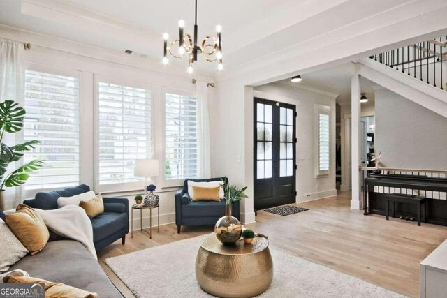 living room with french doors, light hardwood / wood-style floors, an inviting chandelier, and ornamental molding