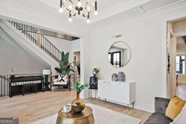 living room featuring crown molding, light hardwood / wood-style floors, and an inviting chandelier