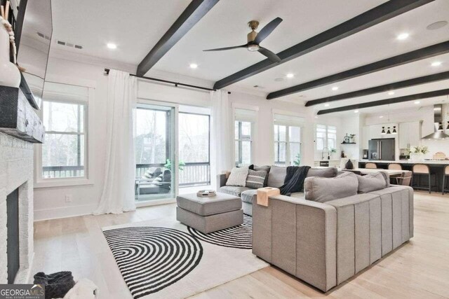 living room featuring beamed ceiling, ceiling fan, a fireplace, and light hardwood / wood-style flooring