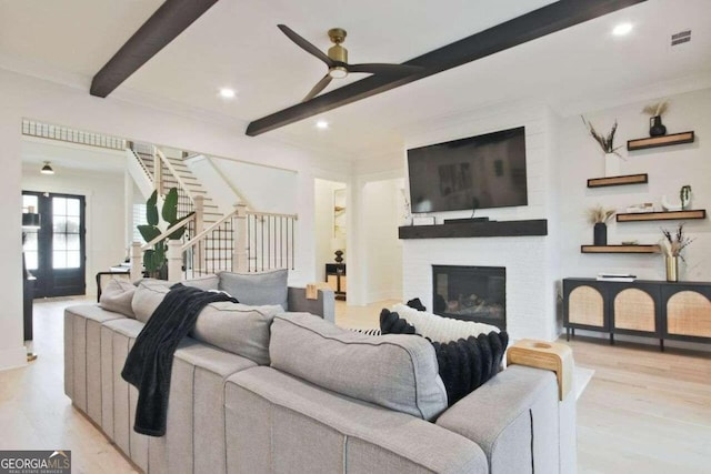 living room with a brick fireplace, ceiling fan, crown molding, beam ceiling, and light hardwood / wood-style floors