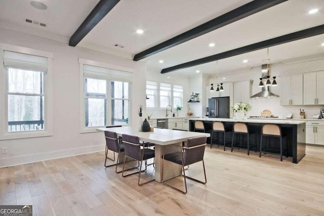 dining area with beam ceiling, light wood-type flooring, a wealth of natural light, and crown molding