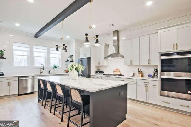 kitchen featuring a center island, wall chimney range hood, decorative light fixtures, white cabinetry, and stainless steel appliances