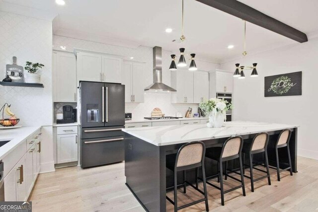 kitchen with white cabinets, a kitchen island, wall chimney range hood, and high quality fridge