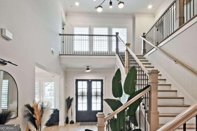 foyer entrance with ornamental molding, light hardwood / wood-style flooring, a towering ceiling, and french doors