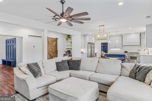 living room with sink, a barn door, built in features, dark hardwood / wood-style floors, and ceiling fan with notable chandelier