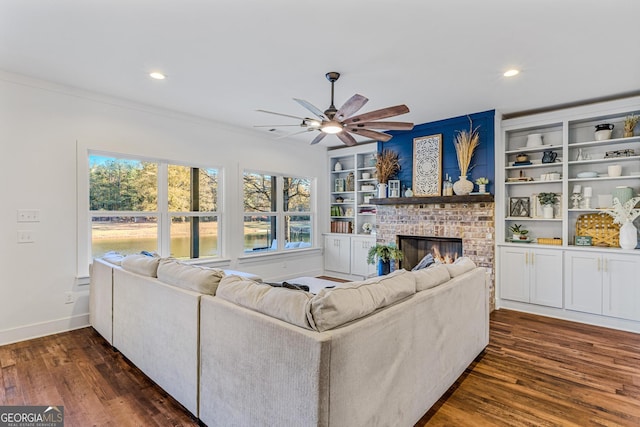 living room featuring dark hardwood / wood-style floors, ceiling fan, ornamental molding, and a fireplace