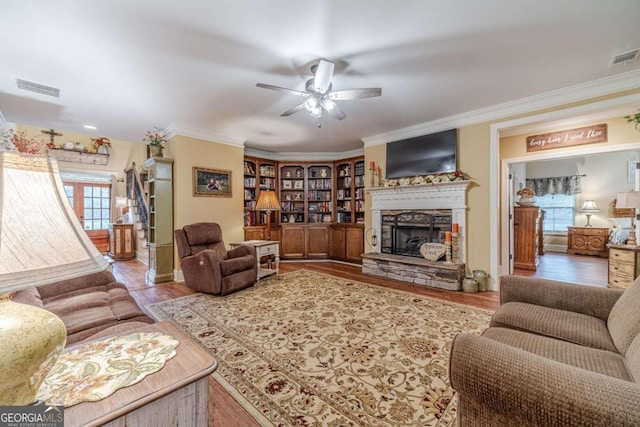 living room featuring hardwood / wood-style flooring, ceiling fan, a stone fireplace, and ornamental molding