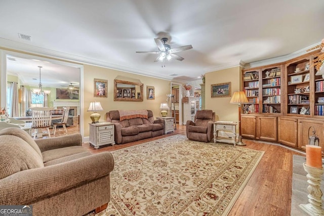 living room with ceiling fan with notable chandelier, light wood-type flooring, and crown molding