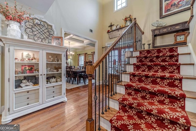 staircase with beamed ceiling, a notable chandelier, wood-type flooring, and a high ceiling