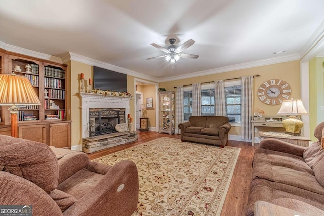 living room with hardwood / wood-style flooring, ceiling fan, ornamental molding, and a fireplace