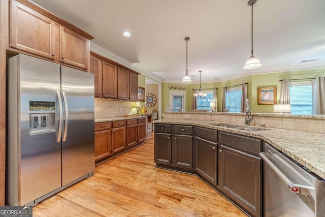 kitchen with sink, tasteful backsplash, decorative light fixtures, appliances with stainless steel finishes, and light wood-type flooring