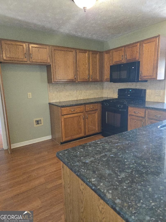 kitchen with backsplash, dark wood-type flooring, black appliances, dark stone countertops, and a textured ceiling