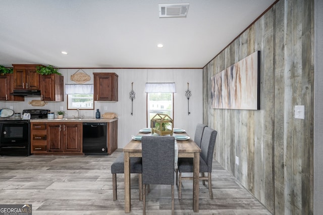 dining room with a wealth of natural light, wooden walls, and light wood-type flooring