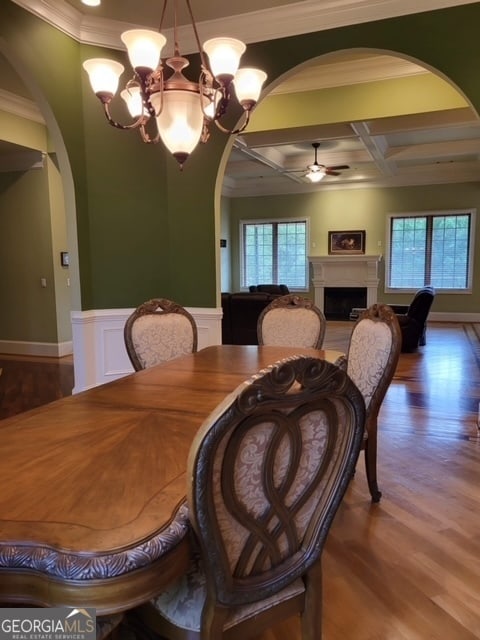 dining space with hardwood / wood-style flooring, ceiling fan with notable chandelier, a wealth of natural light, and coffered ceiling