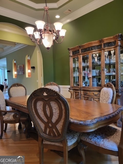 dining area featuring wood-type flooring, crown molding, and a notable chandelier