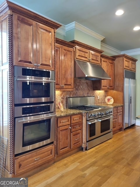 kitchen with appliances with stainless steel finishes, light wood-type flooring, backsplash, ornamental molding, and stone counters