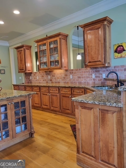 kitchen featuring backsplash, crown molding, sink, stone countertops, and light hardwood / wood-style flooring