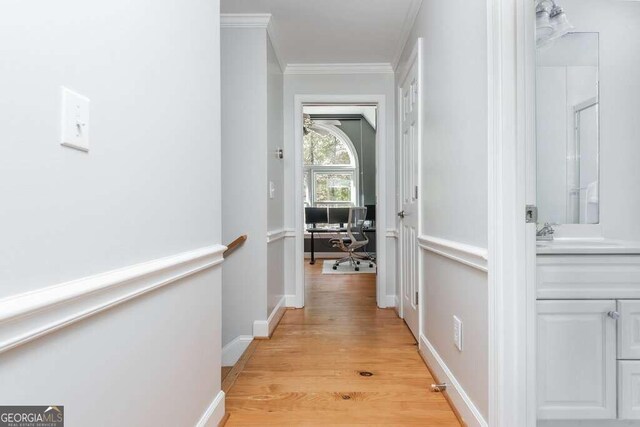 corridor with light wood-type flooring, ornamental molding, and sink