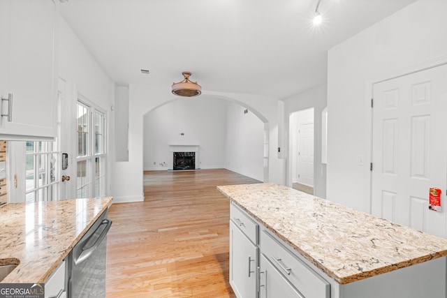 kitchen featuring dishwasher, white cabinetry, a center island, light hardwood / wood-style floors, and light stone countertops