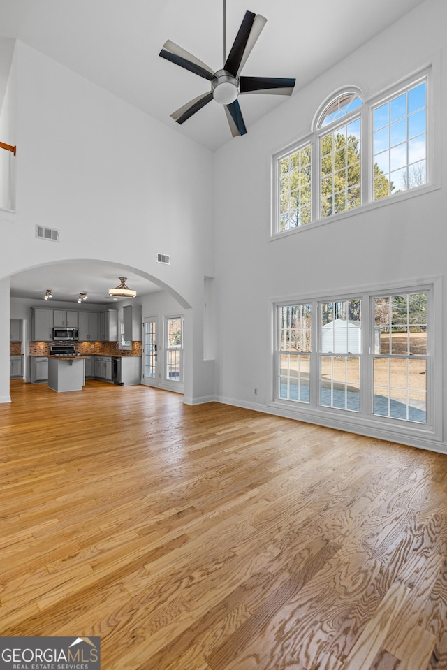 unfurnished living room with light hardwood / wood-style flooring, ceiling fan, and a high ceiling