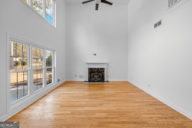 unfurnished living room featuring a towering ceiling, a high end fireplace, ceiling fan, and light wood-type flooring