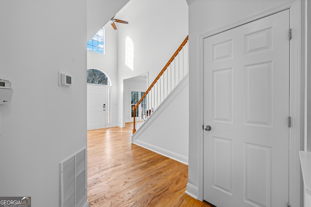 foyer entrance featuring ceiling fan, a towering ceiling, and light wood-type flooring