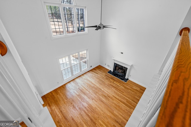 unfurnished living room featuring ceiling fan, a healthy amount of sunlight, a premium fireplace, and light wood-type flooring