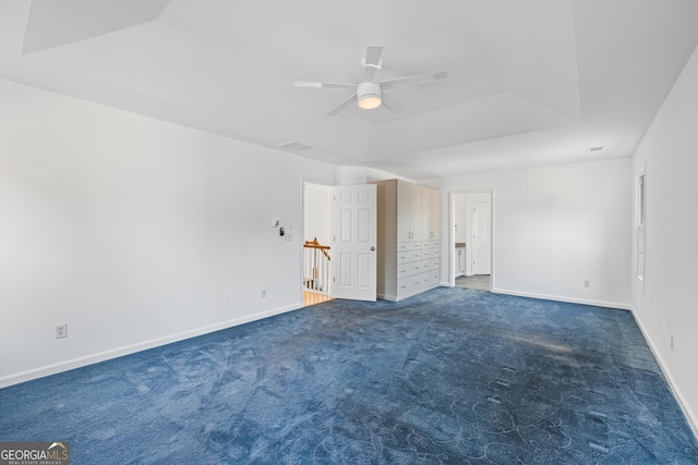 unfurnished room with ceiling fan, a raised ceiling, and dark colored carpet