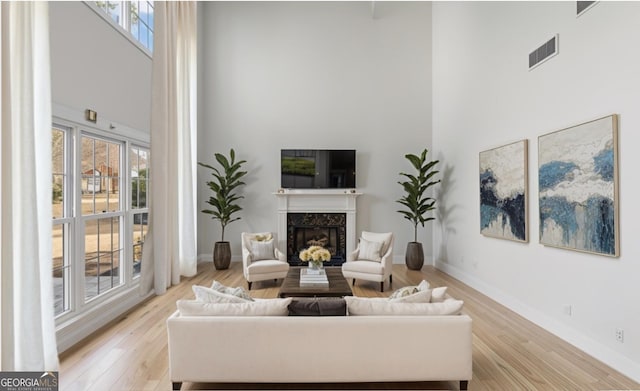 living room with light hardwood / wood-style floors, a healthy amount of sunlight, a fireplace, and a towering ceiling