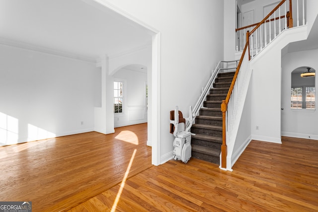 staircase with wood-type flooring, a towering ceiling, and crown molding