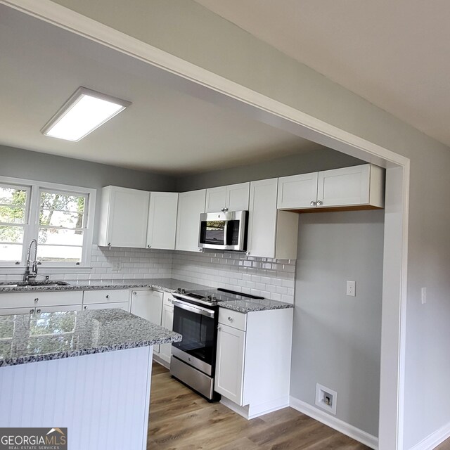 kitchen with appliances with stainless steel finishes, a center island, white cabinetry, and hardwood / wood-style floors