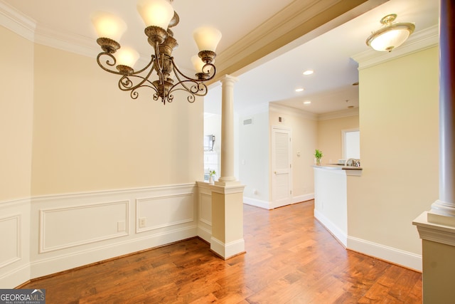 empty room featuring decorative columns, an inviting chandelier, wood-type flooring, and ornamental molding